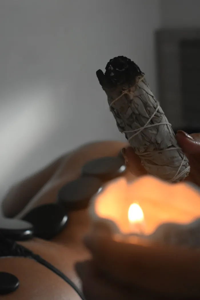 Sahumerio de palo santo encendido junto a una vela, ambiente de ritual y piedras calientes